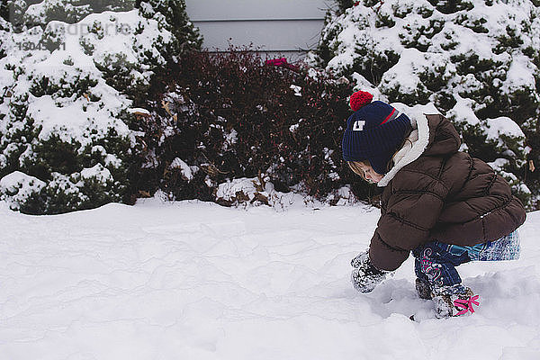 Seitenansicht eines Mädchens  das im Hinterhof mit Schnee spielt