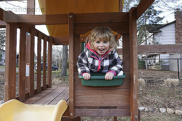 Porträt eines glücklichen Mädchens  das auf einem Spielplatz auf einem Spielgerät im Freien spielt