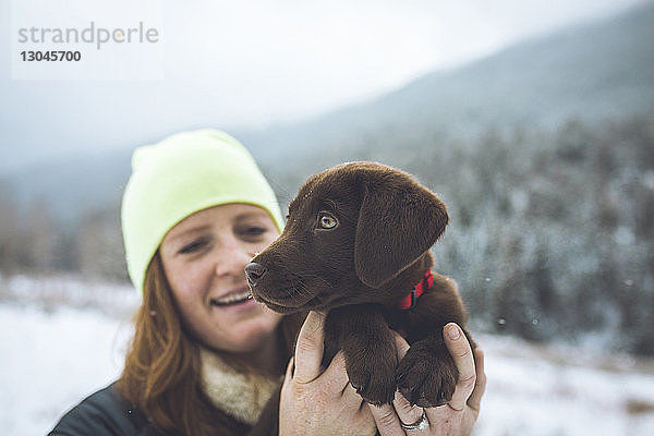 Glückliche Frau mit Schoko-Labrador steht im Winter auf dem Feld