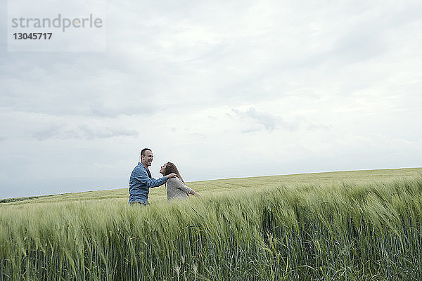 Fröhliches Paar steht im Grasfeld gegen den Himmel