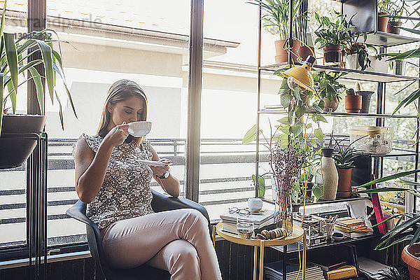 Geschäftsfrau  die Kaffee trinkt  während sie im Home-Office auf einem Stuhl sitzt