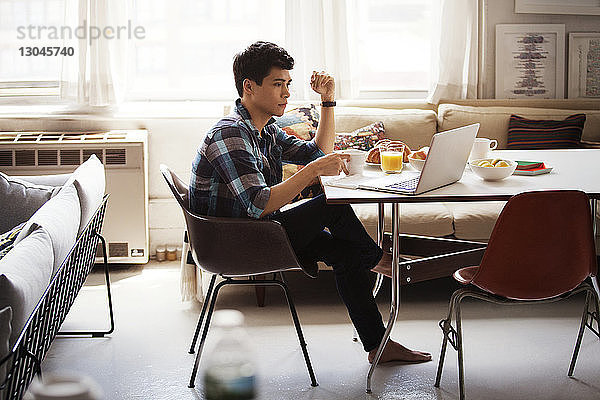 Seitenansicht eines Mannes  der einen Laptop benutzt  während er zu Hause frühstückt