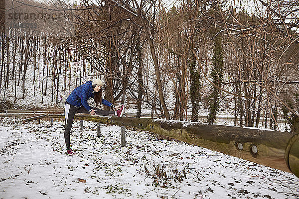 Frau streckt im Winter im Wald ihr Bein auf einer Stange