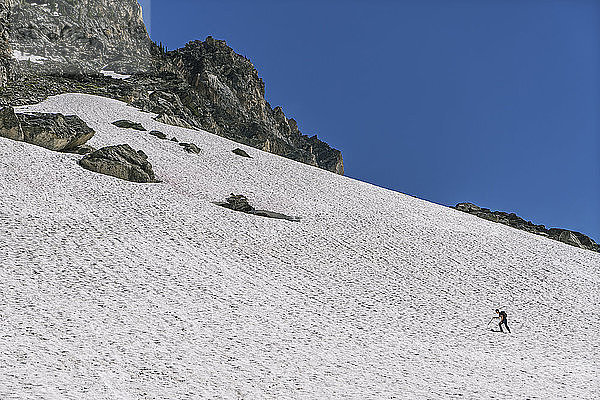 Mitteldistanzansicht eines Mannes  der einen schneebedeckten Berg vor klarem blauen Himmel besteigt