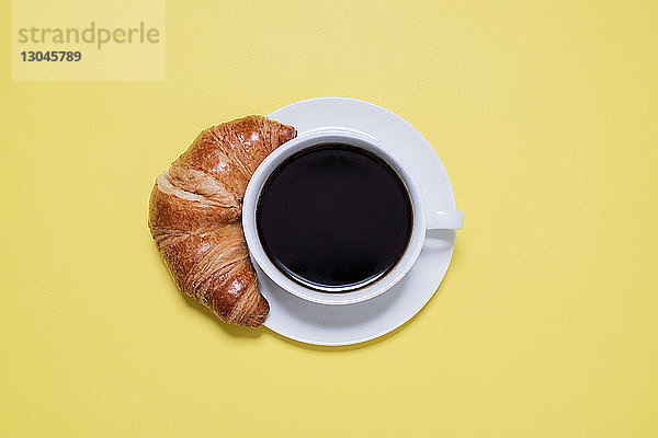 Draufsicht auf schwarzen Kaffee und Croissant auf gelbem Tisch