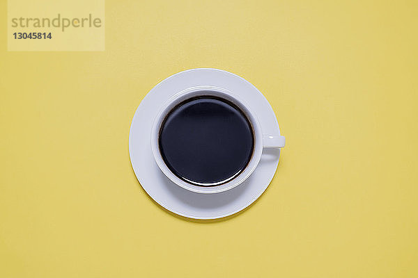 Draufsicht auf schwarzen Kaffee in Tasse auf gelbem Tisch