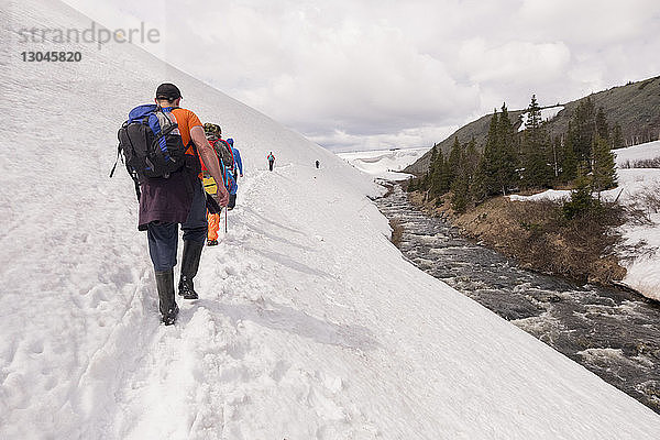 Rückansicht von Wanderern  die auf einem schneebedeckten Hügel vor bewölktem Himmel gehen