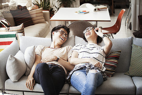 Fröhliches multiethnisches Paar unterhält sich zu Hause auf dem Sofa liegend