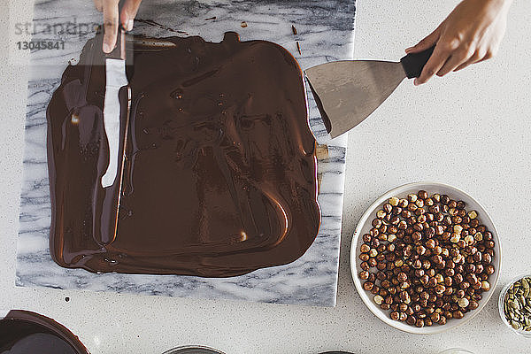 Draufsicht einer Frau  die Schokoladensauce auf Marmor streicht