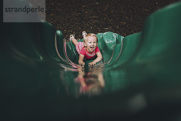 Hochwinkelporträt eines glücklichen Mädchens  das auf einer Rutsche auf einem Spielplatz spielt