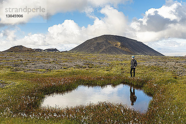Wanderer steht am Teich auf dem Feld vor Bergen und bewölktem Himmel