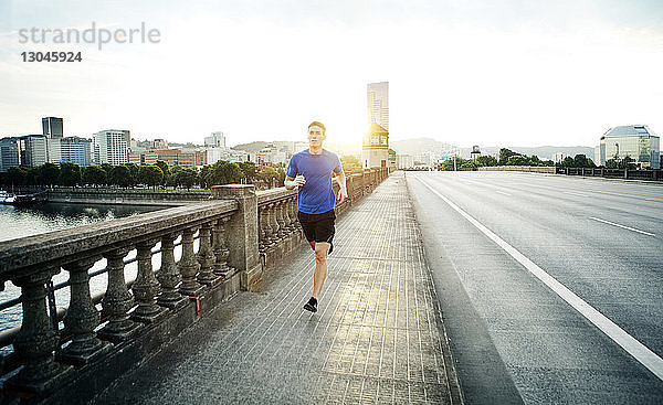 Sportlicher Mann joggt auf Fußweg gegen den Himmel in der Stadt
