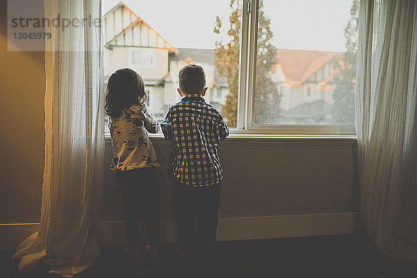 Rückansicht der Geschwister  die zu Hause am Fenster stehen