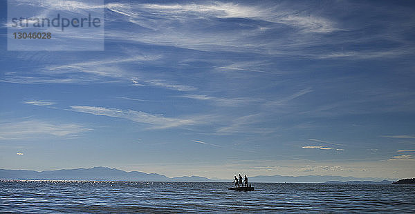Silhouetten von Menschen  die auf einer schwimmenden Plattform im Meer gegen den Himmel stehen
