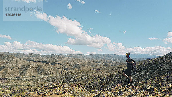 Männlicher Wanderer mit Rucksack  der am sonnigen Tag auf dem Feld gegen den Himmel läuft