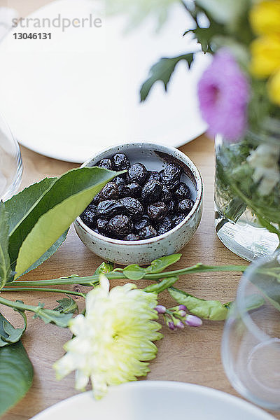 Hochwinkelansicht von Datteln in Schale durch Blumen auf Holztisch