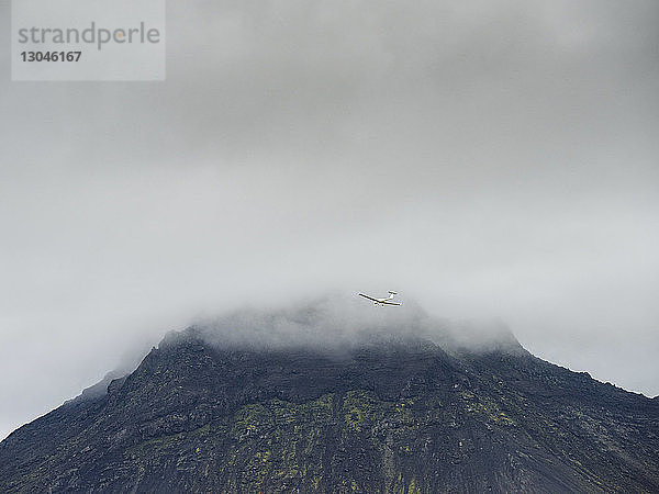 Niedrigwinkelansicht eines Spielzeugflugzeugs  das gegen Berg und Wolkenhimmel fliegt