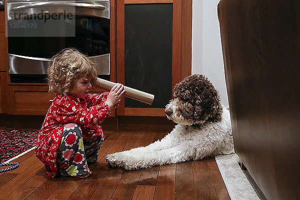 Verspieltes Mädchen schaut durch Pappröhre auf Hund