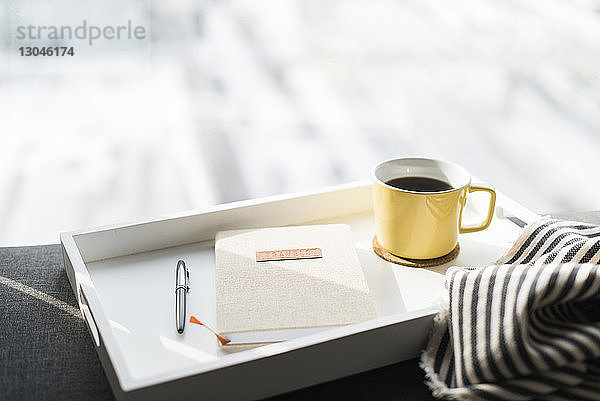 Nahaufnahme des Tagebuchs zwischen Stift und Kaffeetasse im Tablett auf dem Sofa