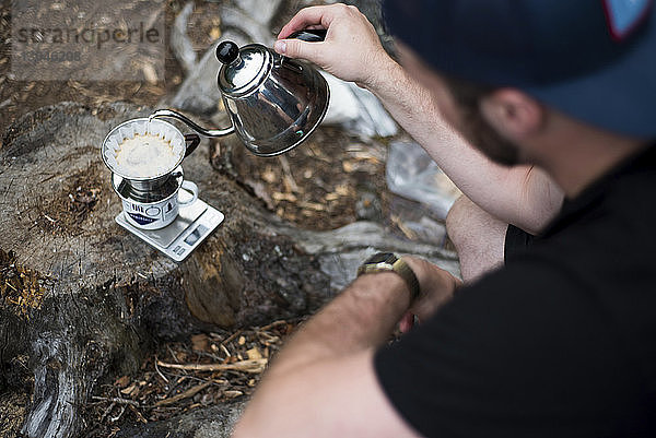 Schrägaufnahme eines Mannes  der auf dem Campingplatz Kaffee in den Filter gießt