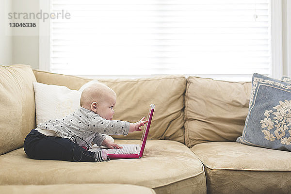 Seitenansicht eines kleinen Mädchens  das zu Hause auf dem Sofa sitzend mit einem Laptop-Computer spielt