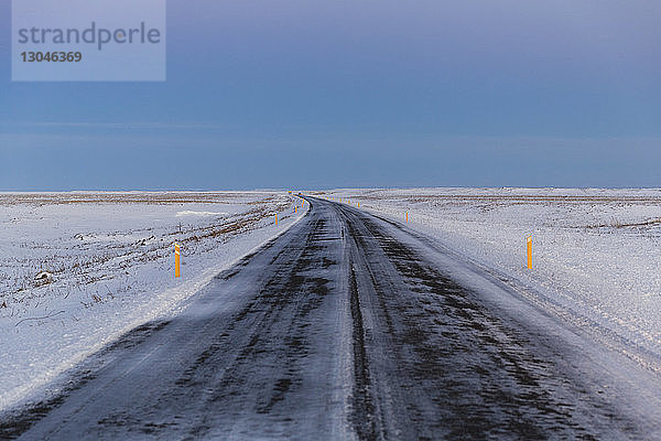 Landstraße inmitten eines verschneiten Feldes gegen den Himmel