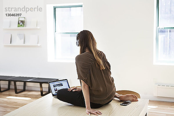 Rückansicht einer Geschäftsfrau  die einen Laptop benutzt  während sie im Kreativbüro am Schreibtisch sitzt