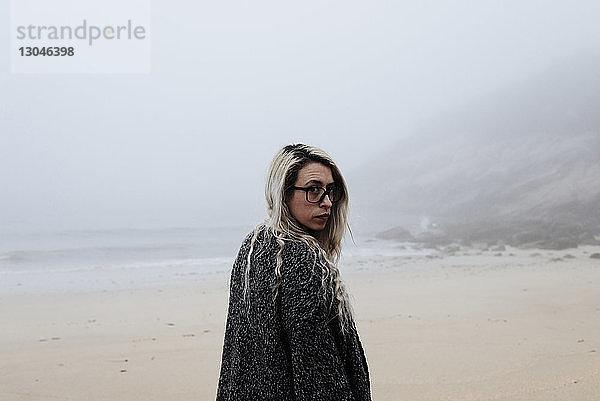 Porträt einer Frau  die bei nebligem Wetter am Strand steht