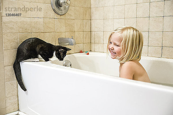 Fröhliches Mädchen mit Katze in der Badewanne
