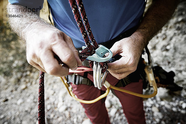 Mittelteil eines männlichen Wanderers  der ein Kletterseil am Berg justiert