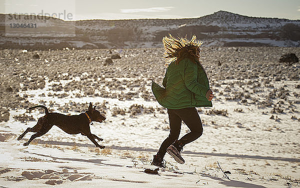 Glückliche Frau spielt mit Hund auf schneebedecktem Feld