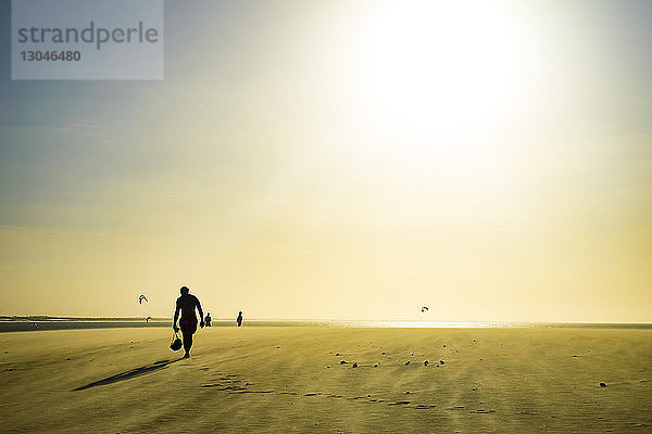 Silhouetten von Menschen  die auf Sand gegen den Himmel laufen