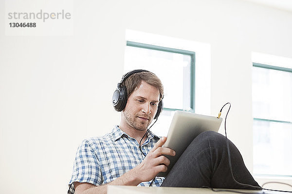 Geschäftsmann mit Tablet-Computer beim Musikhören im Büro