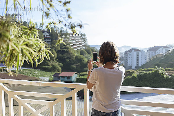 Rückansicht einer Frau  die mit einem Smartphone fotografiert  während sie in der Stadt am Geländer steht
