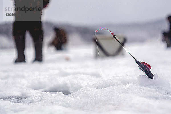 Angelrute durch Loch auf Schnee mit Frau im Hintergrund