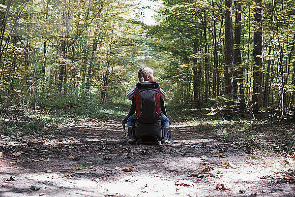 Rückansicht eines auf einer Tasche sitzenden Mädchens mit Rucksack auf einem Feldweg mitten im Wald
