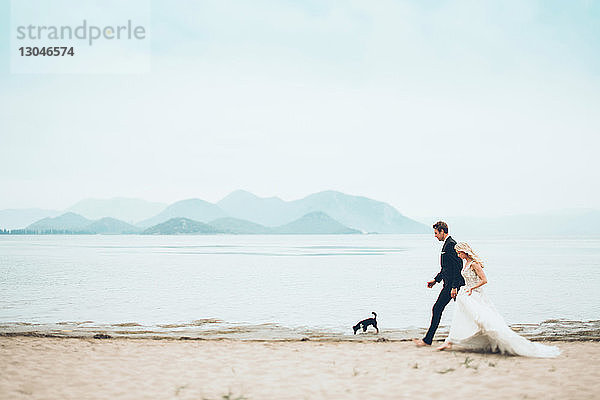 Brücke und Bräutigam mit Hund beim Spaziergang am Strand gegen den Himmel