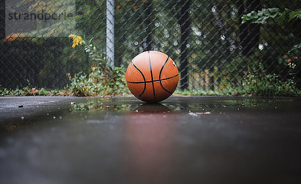 Nahaufnahme des Balls auf nassem Basketballfeld gegen den Maschendrahtzaun