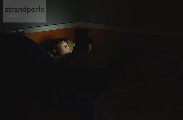 Junge benutzt Tablet-Computer  während er zu Hause in der Dunkelkammer auf dem Bett liegt