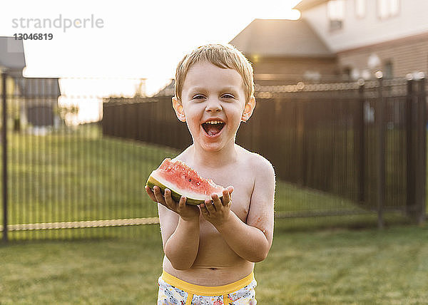 Porträt eines fröhlichen Jungen  der im Hinterhof eine Wassermelone isst