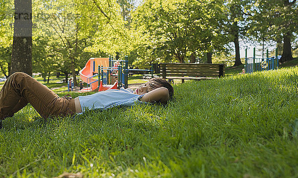 Seitenansicht eines Jungen  der auf einem Grasfeld im Park liegt