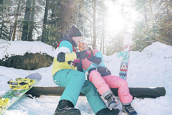 Verspieltes Paar sitzt im Winter auf einem Baumstamm im Wald