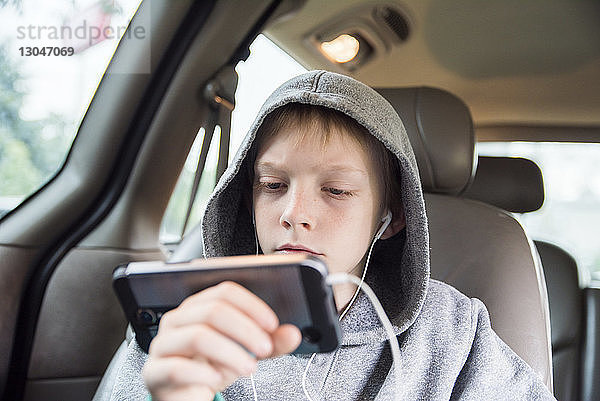 Junge mit Kapuzenhemd  der ein Smartphone benutzt  während er im Auto sitzt
