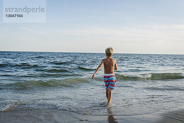 Rückansicht eines Jungen ohne Hemd  der am Tobay Beach in Richtung Meer gegen den Himmel läuft