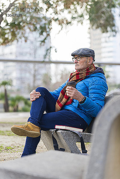 Nachdenklicher Mann mit Kaffee und Buch auf Parkbank sitzend