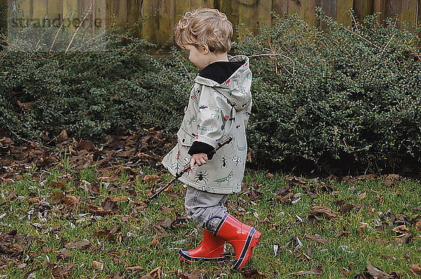Junge in voller Länge mit Stock in der Hand  während er im Herbst im Hinterhof spazieren geht