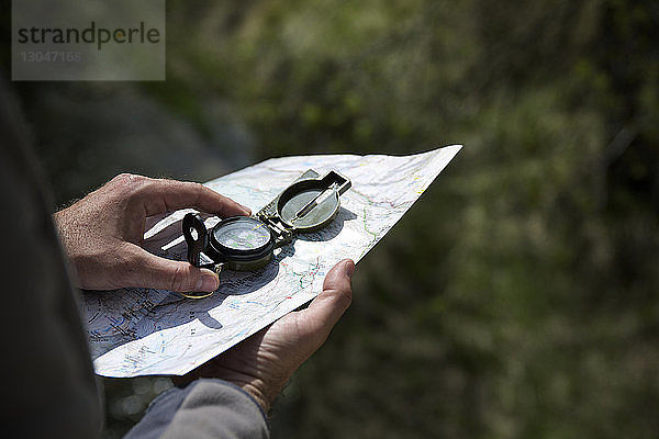 Abgehackte Hände eines männlichen Wanderers mit Navigationskompass und Karte im Wald