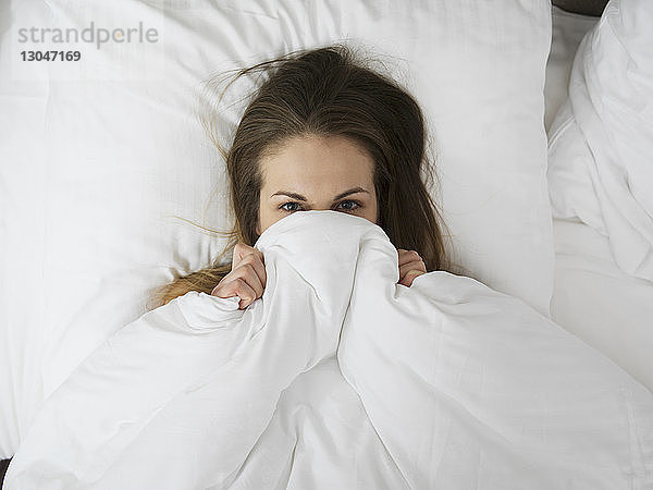 Draufsicht auf eine Frau  die sich in einer Decke auf dem Bett versteckt