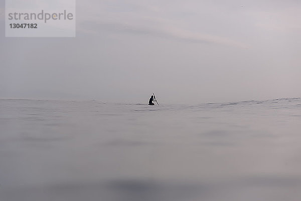 Mitteldistanzansicht des Silhouettenmannes beim Paddeln im Meer gegen den Himmel