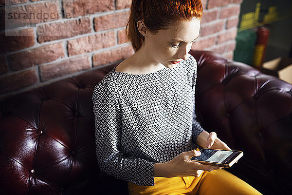 Schrägansicht einer Geschäftsfrau mit einem Smartphone auf der Couch im Büro